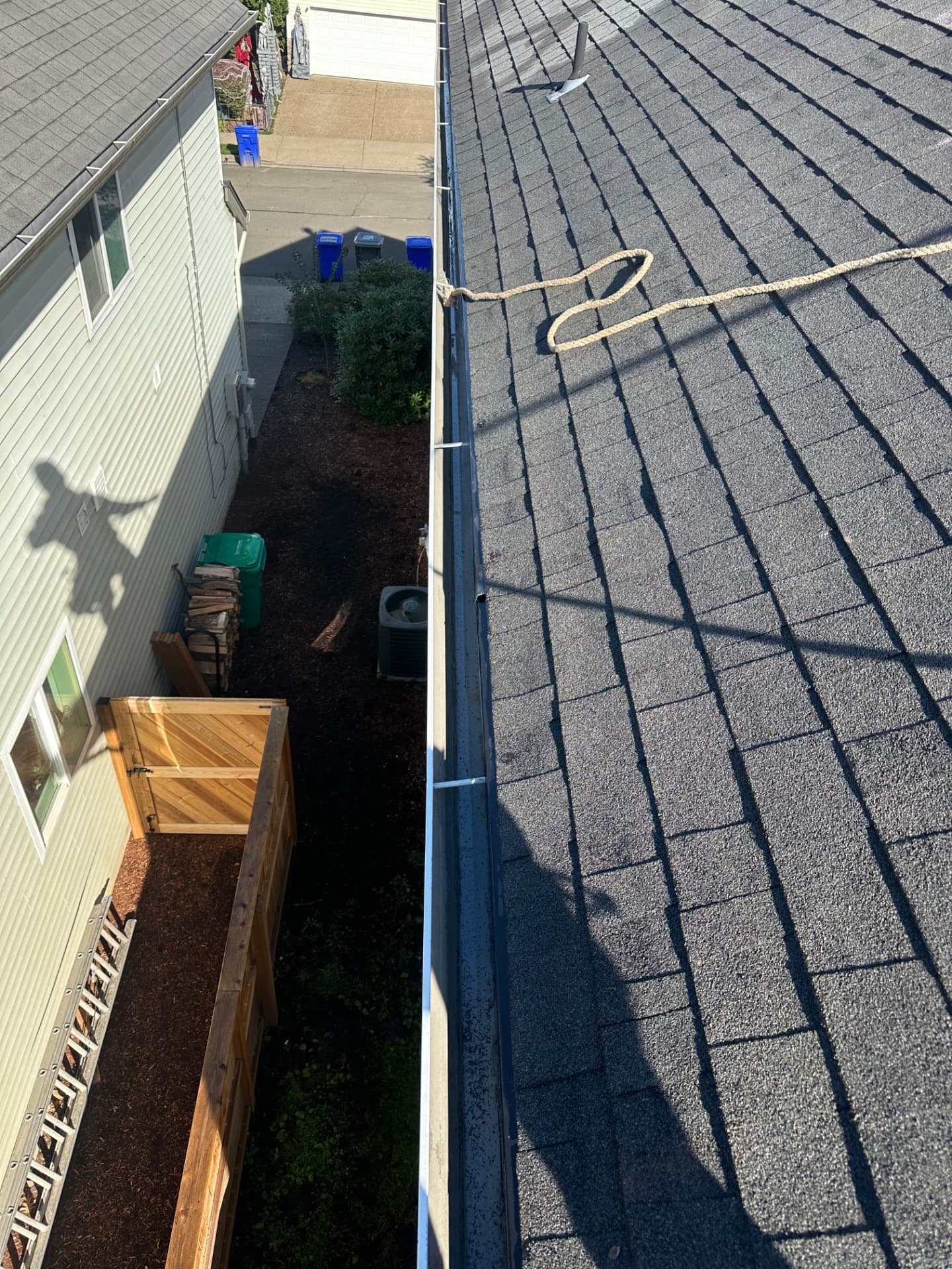 Cleaned gutters along the edge of an asphalt shingle roof, viewed from the rooftop