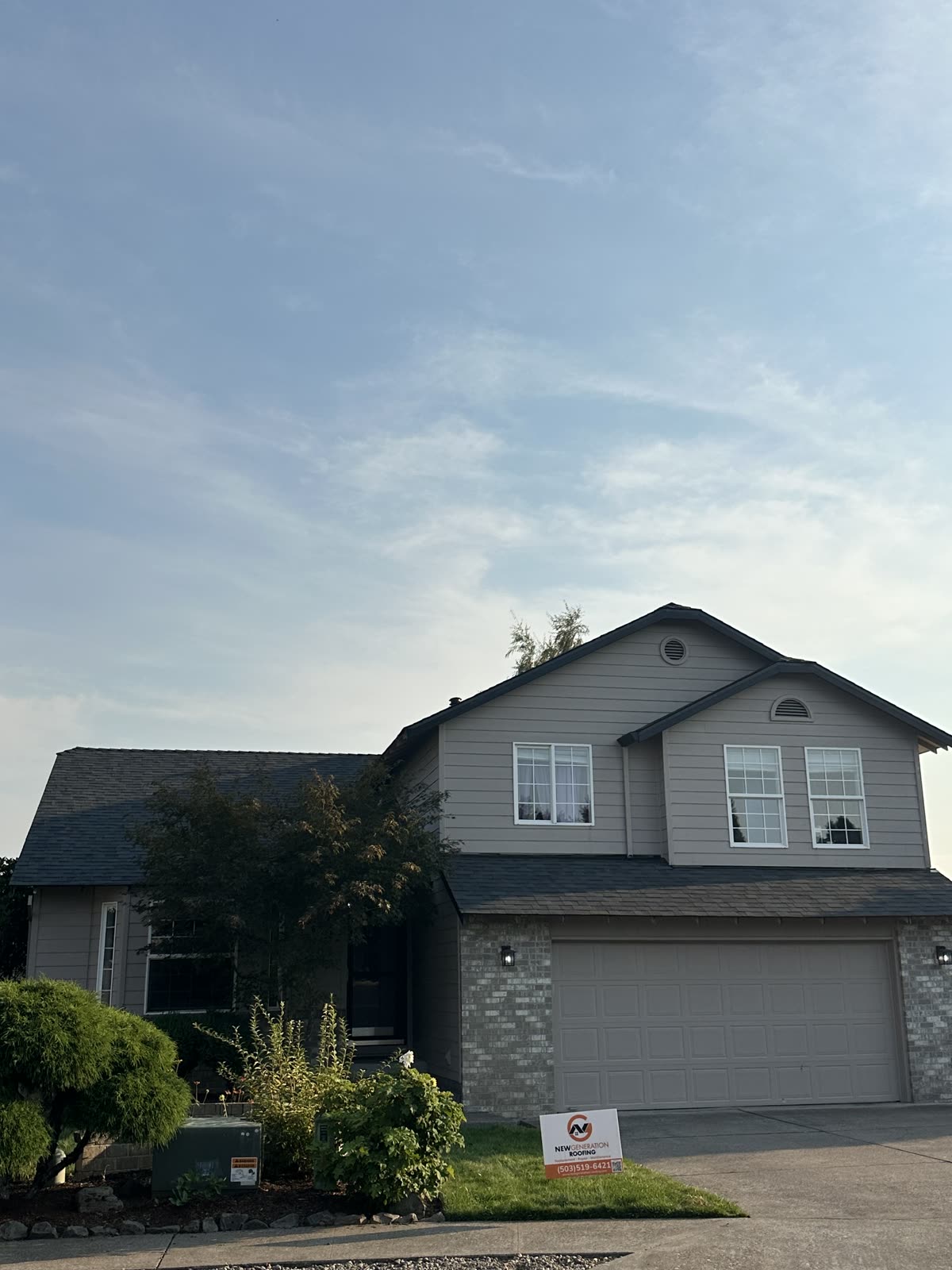Newly replaced asphalt shingle roof on a two-story home with a New Generation Roofing sign in the front yard