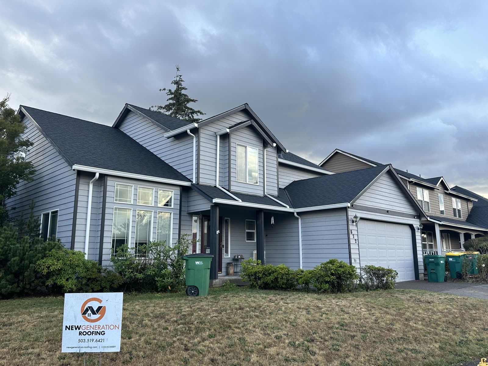 Completed dark asphalt shingle roof replacement on a gray two-story home with a New Generation Roofing yard sign